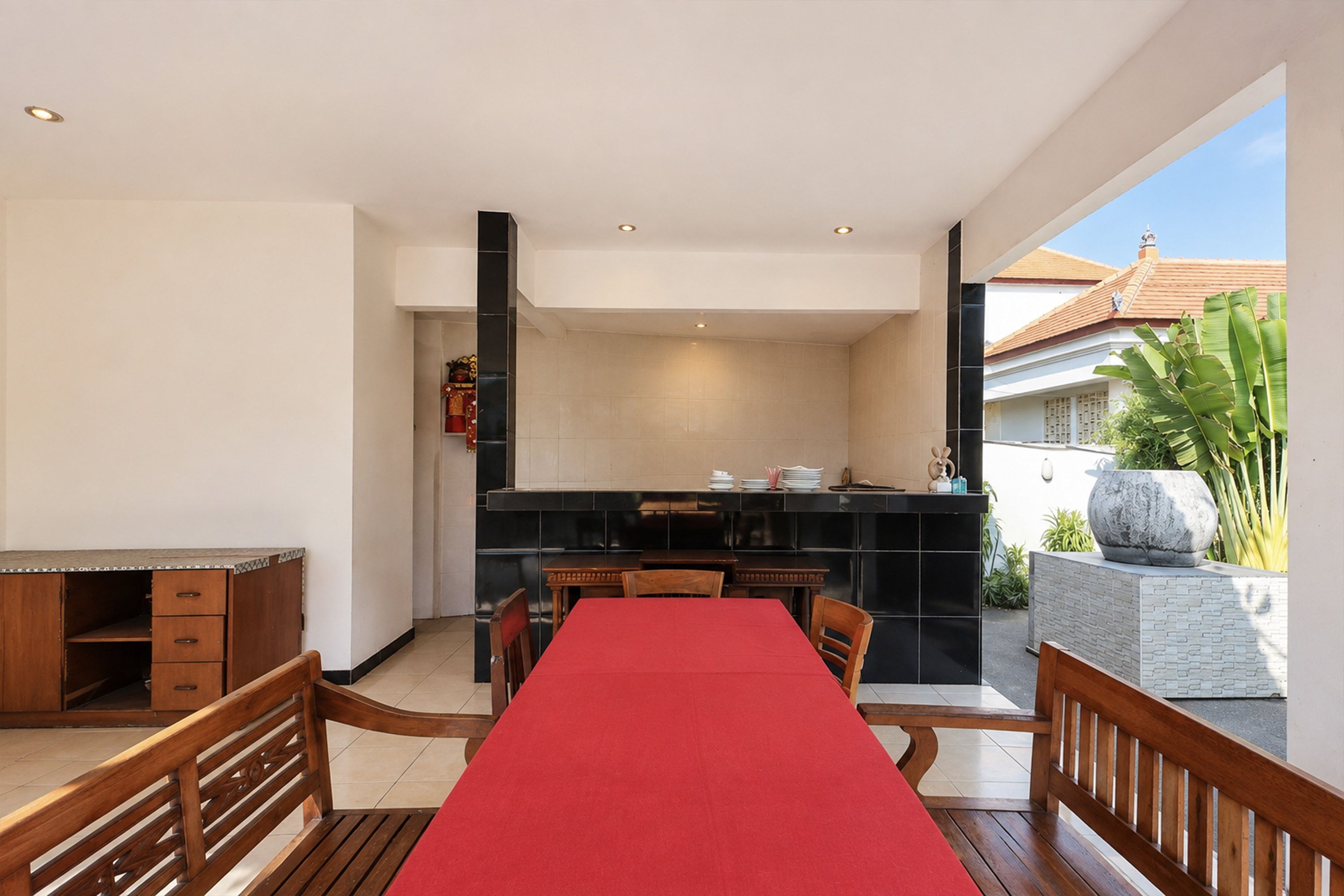 Un coin repas avec une nappe rouge, des chaises en bois et une cuisine en arrière-plan.
