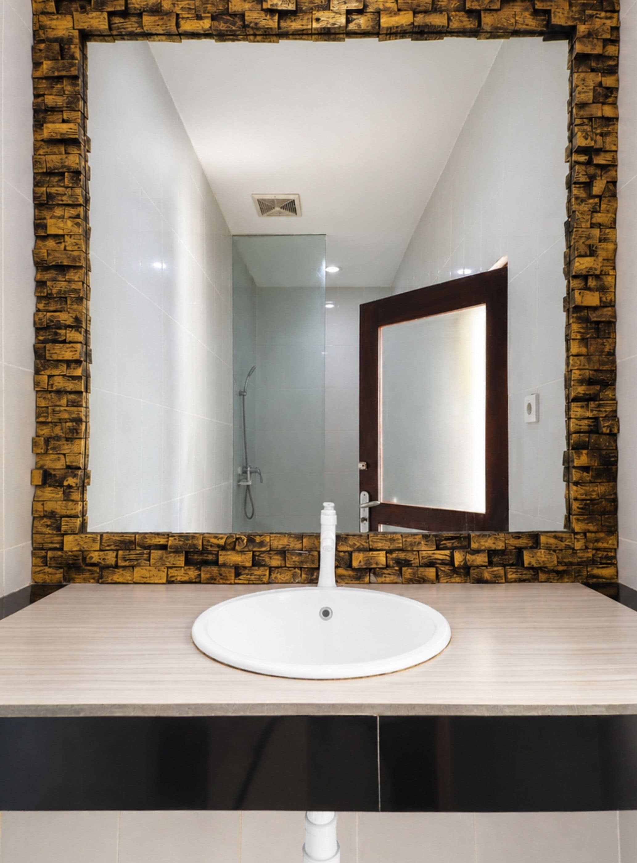 A bathroom with a stone-framed mirror, a white sink, and a shower area.