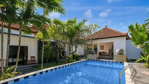 A swimming pool with a tiled deck, surrounded by palm trees and a building with a tiled roof. - Collection O near Pantai Nusadua formerl (Nusa Dua)