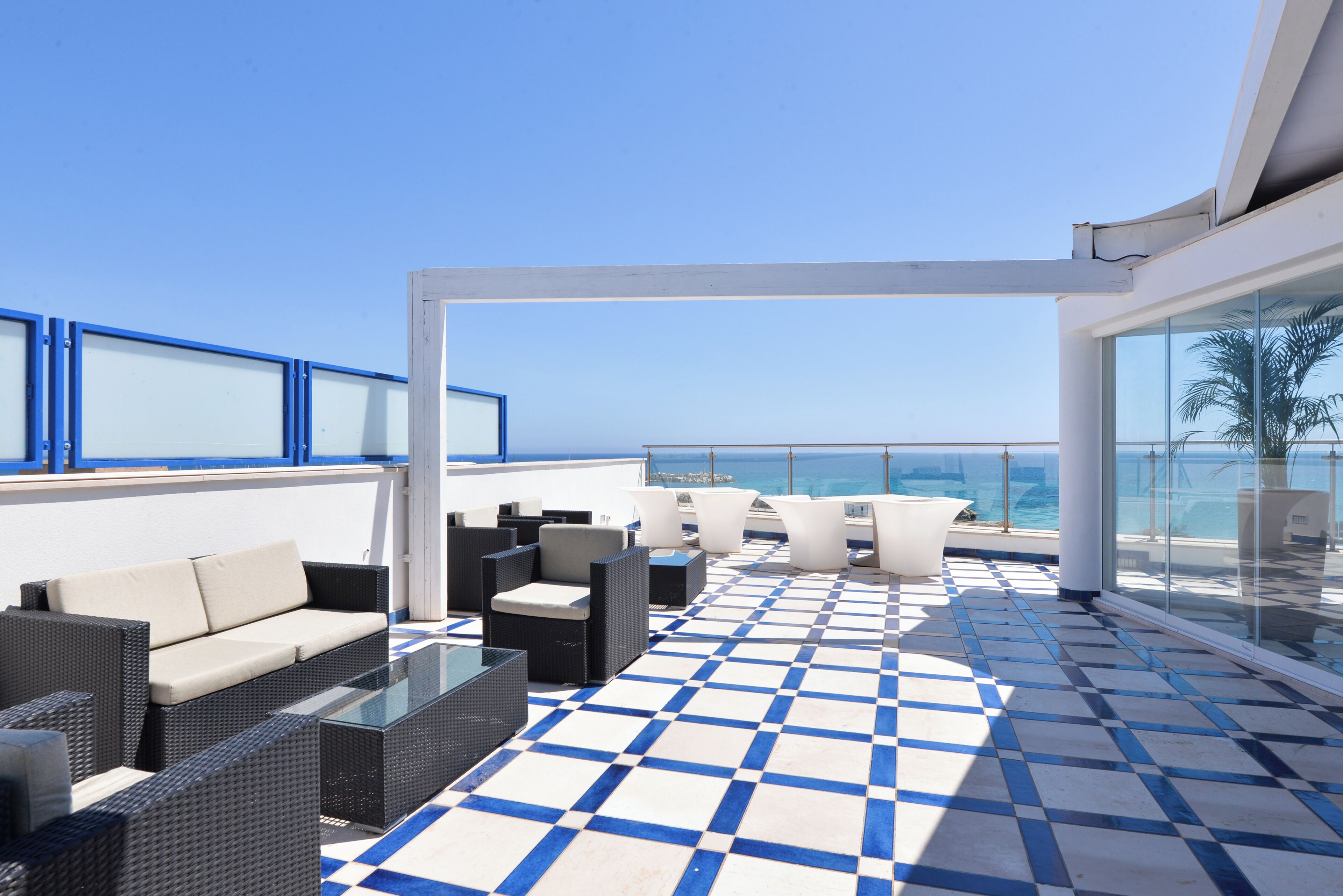 A rooftop terrace with outdoor seating, a checkered floor, and a view of the sea.