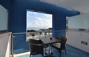 A balcony with a view of the sea, a table, and two chairs.