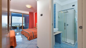 A hotel room with a balcony, a bed with a striped bedspread, a bathroom with a glass shower enclosure, and a view of the sea. - Damavi Hotel (San Foca)