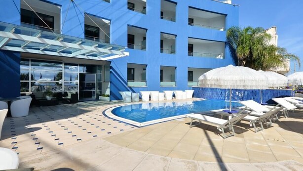 A modern hotel with a swimming pool, outdoor seating, and a clear blue sky. - Damavi Hotel (San Foca)