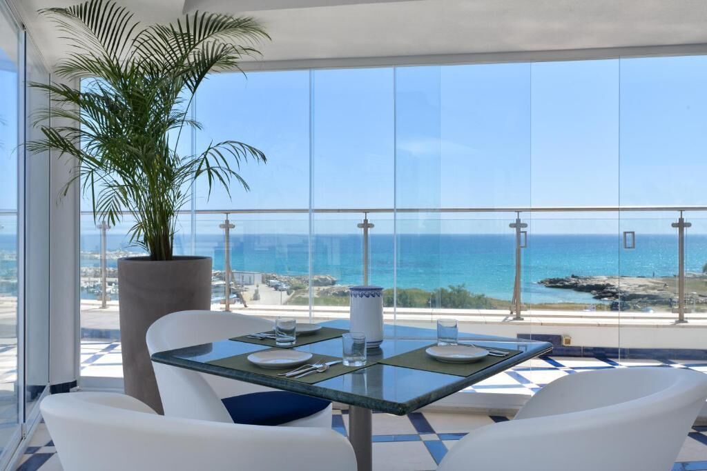 A balcony with a table set for two, overlooking a coastal view.