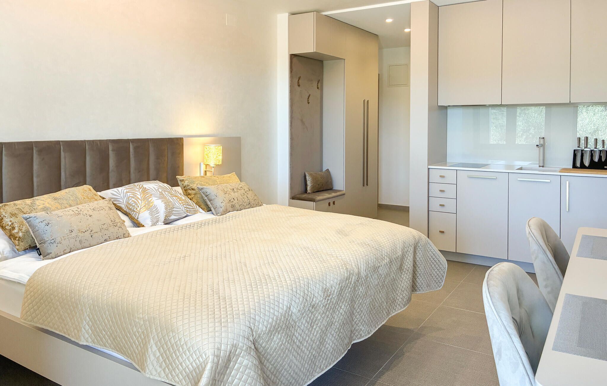 A modern bedroom with a large bed, bedside table, and a built-in kitchenette.