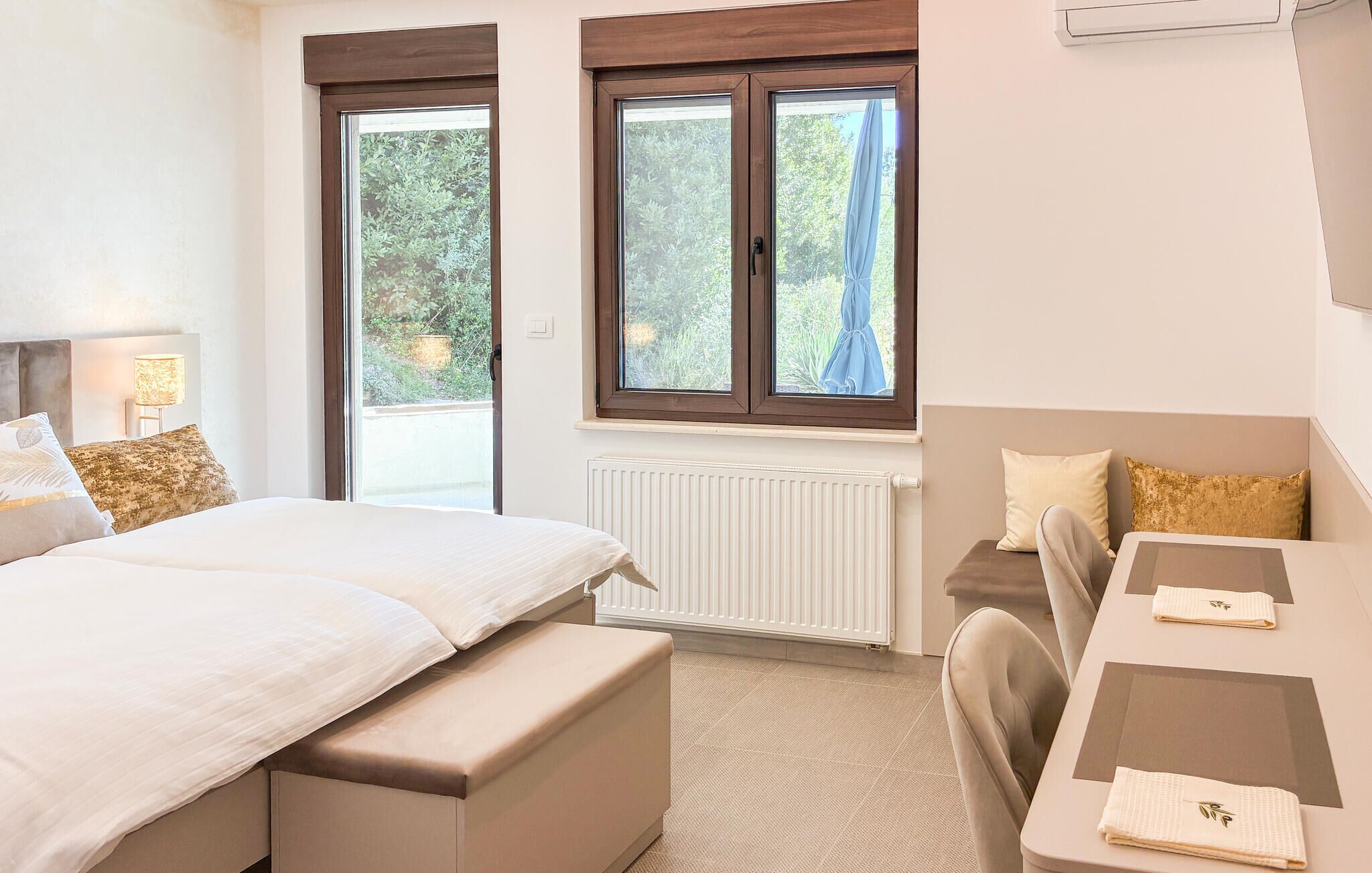 A bedroom with a bed, a desk, and a chair. There is a window with a view of greenery outside.