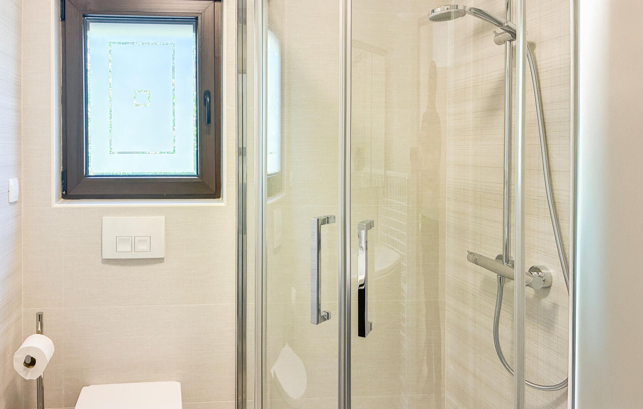 Une salle de bain avec une douche à parois de verre, des toilettes, un distributeur d’essuie-tout et une fenêtre donnant sur un beau paysage.