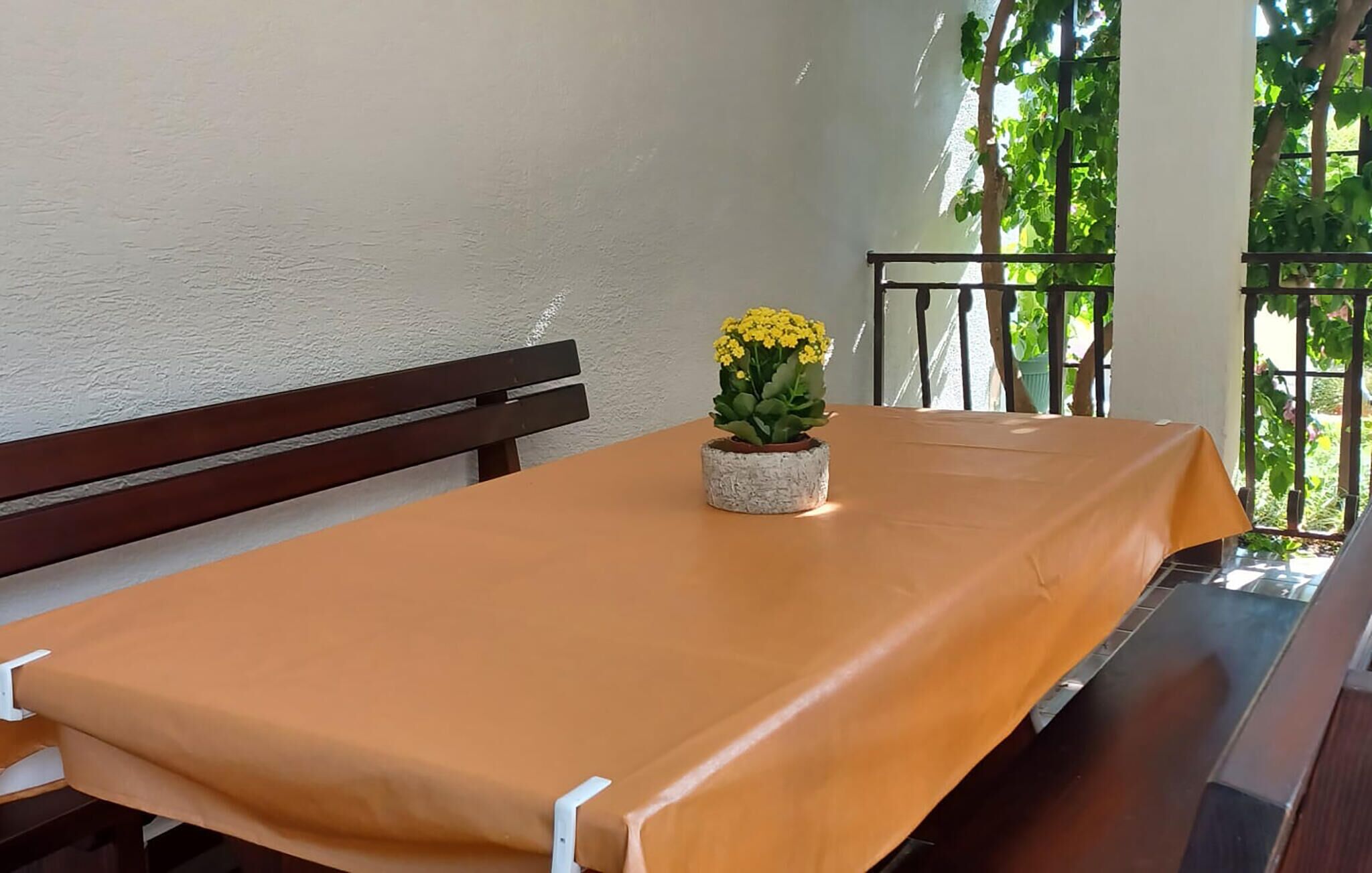 A table with a yellow tablecloth, a bench, and a potted plant with yellow flowers.