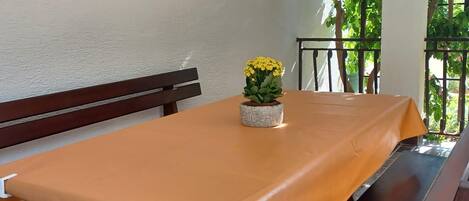 A table with a yellow tablecloth, a bench, and a potted plant with yellow flowers.