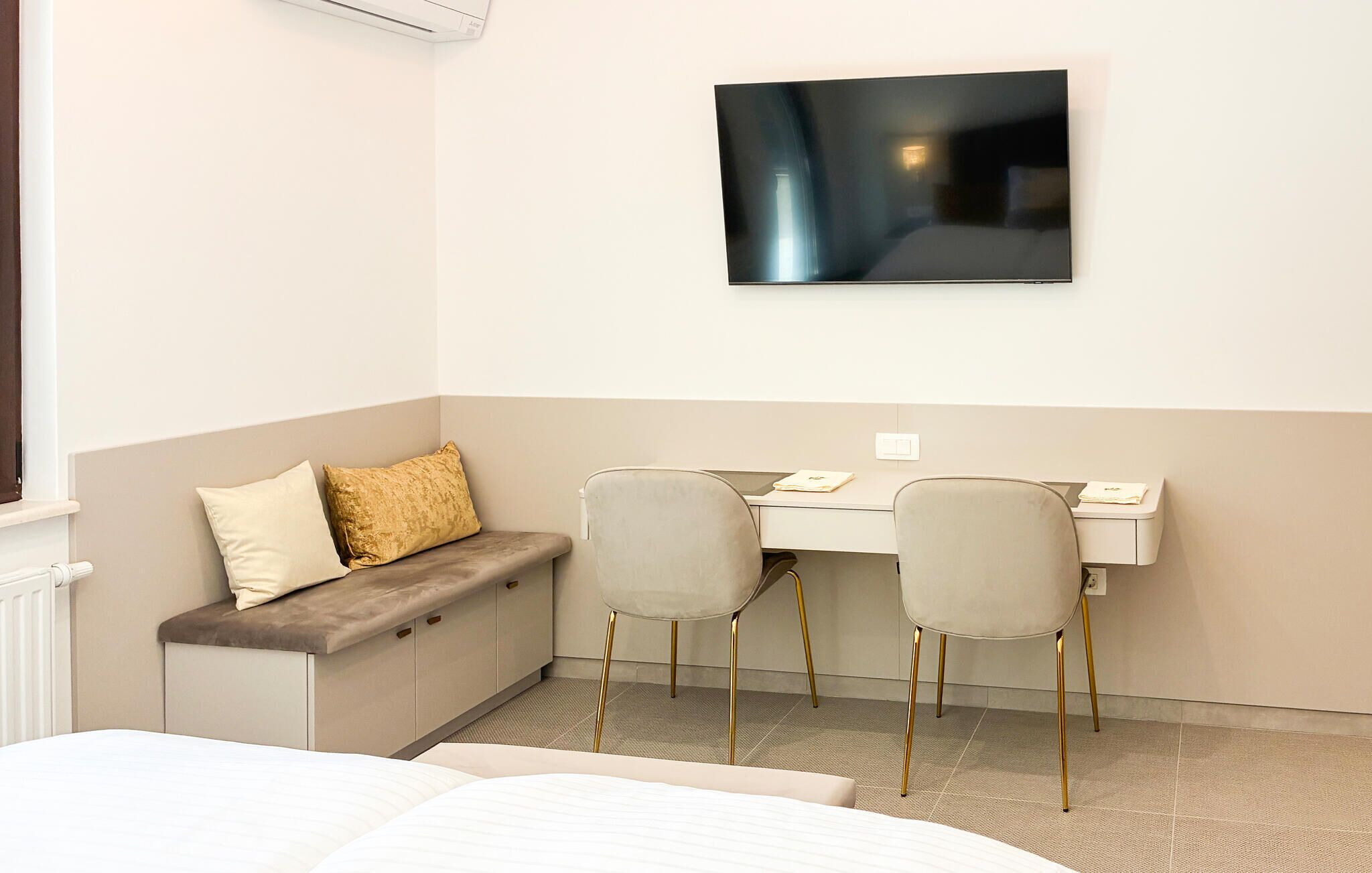A hotel room with a bed, a desk, two chairs, a TV mounted on the wall, and a window.