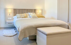 Ein modernes Schlafzimmer mit Bett, Nachttischlampen, einem Nachttisch und einer Bank.