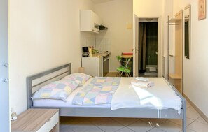 Ein Schlafzimmer mit Bett, Nachttisch, kleinem Schreibtisch, Stuhl, einem Badezimmer mit Dusche und einer Küchenzeile.