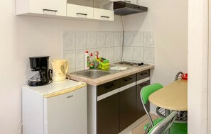 Eine kompakte Küchenzeile mit Kaffeemaschine, Spüle und einer kleinen Essecke mit einem Stuhl.