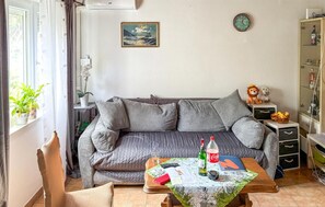Ein gemütliches Wohnzimmer mit einem grauen Sofa, einem kleinen Tisch mit einer Flasche, einer Fernbedienung und einem Buch.