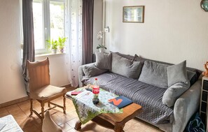 Ein gemütliches Wohnzimmer mit einer Couch, einem Holzstuhl, einem Tisch mit einer Flasche und einem gerahmten Bild an der Wand.