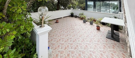 Terraza en la azotea con plantas en macetas, barandilla de cristal y una mesa blanca.