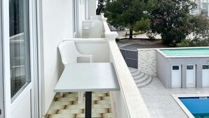 A balcony with a white table and chairs, a pool, and a stone wall. - Nice apartment in Rab with WiFi (Rab)