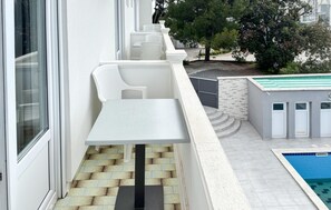 A balcony with a white table and chairs, a pool, and a stone wall. - Nice apartment in Rab with WiFi (Rab)