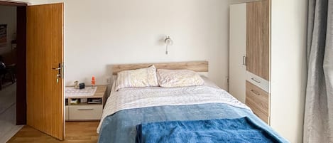 Un dormitorio con cama, mesita de noche, lámpara, armario y una puerta abierta que da a otra habitación.