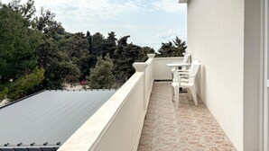 A balcony with a table and chairs, a view of trees and a red car, and a tiled floor. - Nice apartment in Rab with WiFi (Rab)