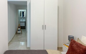 Ein Schlafzimmer mit Bett, Kleiderschrank, Schreibtisch mit Lampe und Blick ins Badezimmer.