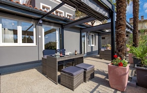 Eine Terrasse im Freien mit Korbmöbeln, einem Tisch mit Flasche und Glas sowie Topfpflanzen.