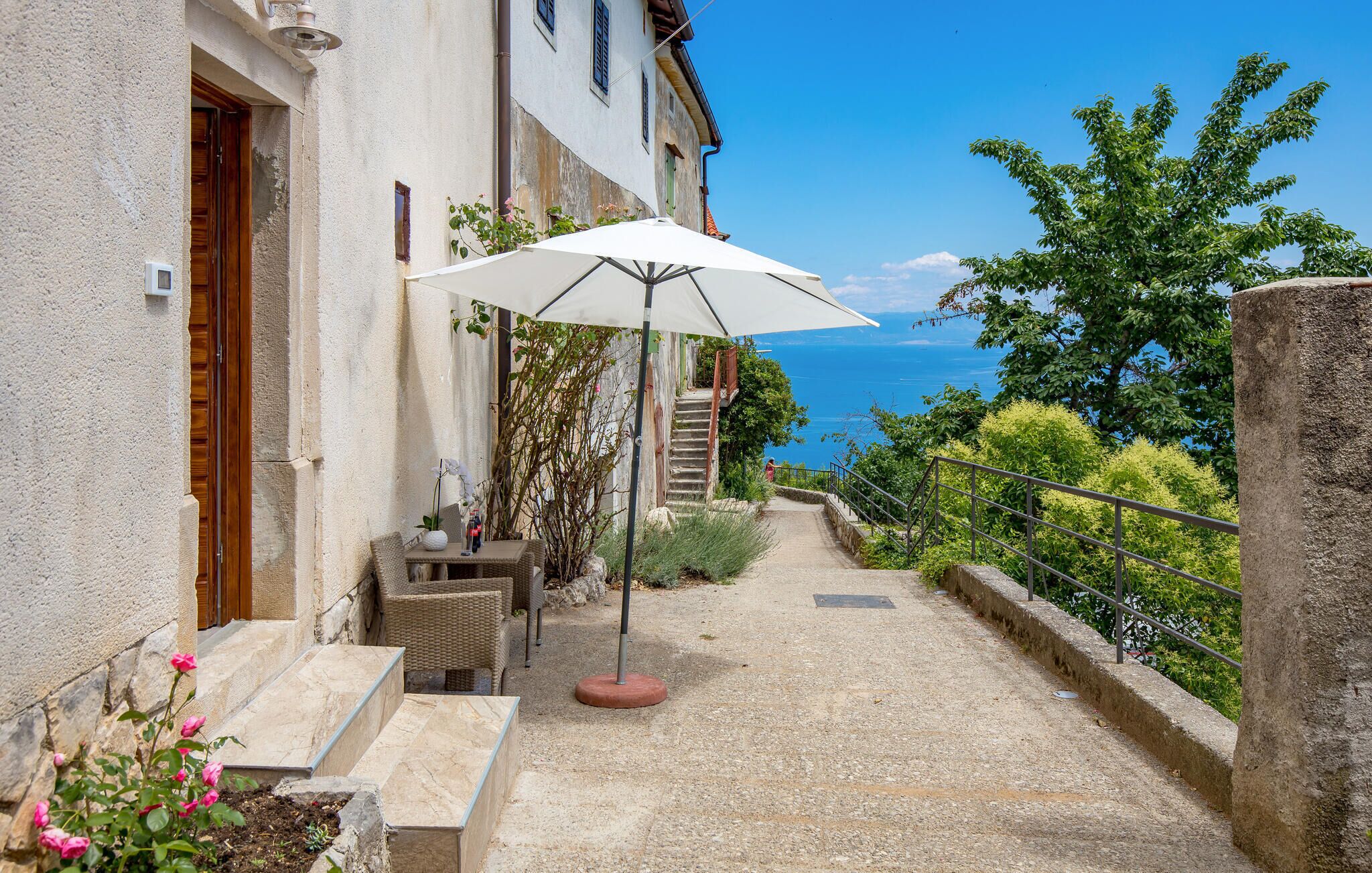 Eine Terrasse mit Gartenmöbeln, einem weißen Sonnenschirm und Blick aufs Meer.