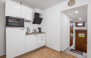 Eine kompakte Küche mit weißen Schränken, einer eingebauten Mikrowelle, einem Wasserkocher und einer Holz Arbeitsplatte.