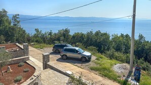 Una propietat a la costa amb dos cotxes aparcats, un camí de pedra i vistes al mar i a les muntanyes.