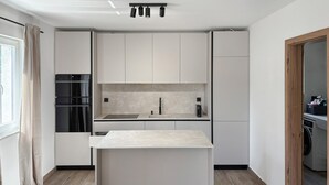 Una cuina moderna amb una illa central, electrodomèstics integrats i vista a l'habitació veïna.