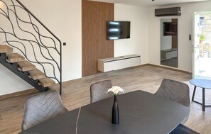 A modern living room with a staircase, a flat-screen TV mounted on the wall, a dining table with chairs, and a vase with a flower. - Stunning home in Opatija-Moscenicka (Opatija-Moscenicka)