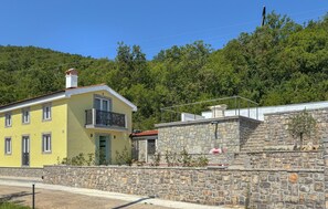 A yellow building with a balcony, a stone wall, and a forested hillside in the background. - Stunning home in Opatija-Moscenicka (Opatija-Moscenicka)