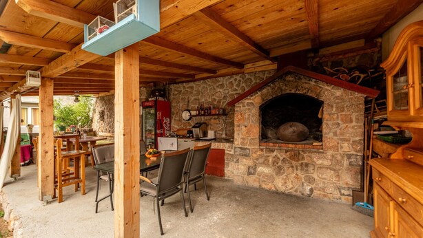 An outdoor patio with a stone fireplace, wooden furniture, and a Coca-Cola refrigerator. - Gorgeous apartment in Karlobag with WiFi (Karlobag)