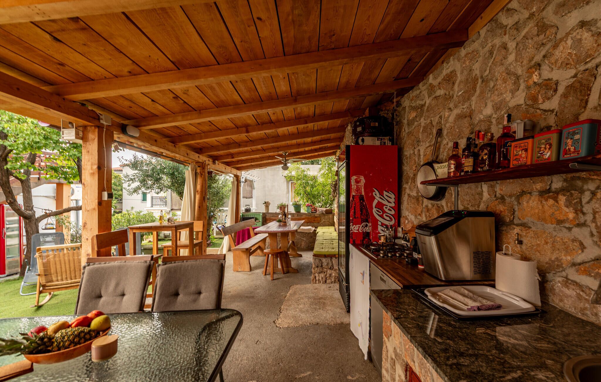 A covered outdoor dining area with wooden furniture and a stone wall.
