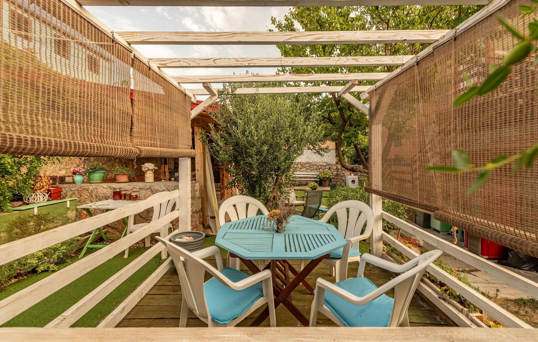 An outdoor patio with a table and chairs, surrounded by a wooden fence and covered by a woven canopy.