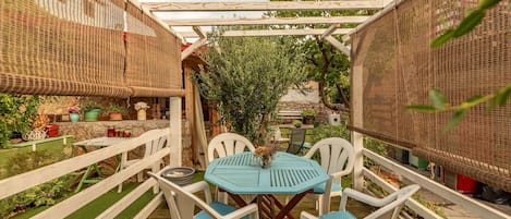 An outdoor patio with a table and chairs, surrounded by a wooden fence and covered by a woven canopy.