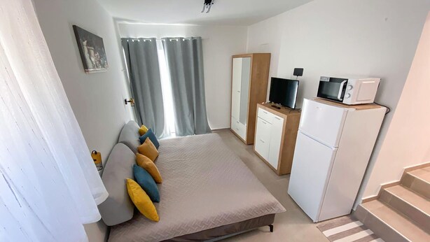 A bedroom with a bed, a television, a refrigerator, and a bathroom with a shower curtain. - Lovely apartment in Karlobag with WiFi (Karlobag)