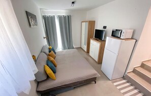Ein Schlafzimmer mit einem Bett, einem Fernseher, einem Kühlschrank und einem Badezimmer mit Duschvorhang.