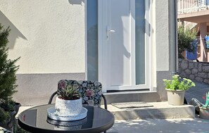 Ein Sitzbereich im Freien mit Tisch und Stühlen, einem Blumentopf und einer Tür im Hintergrund.
