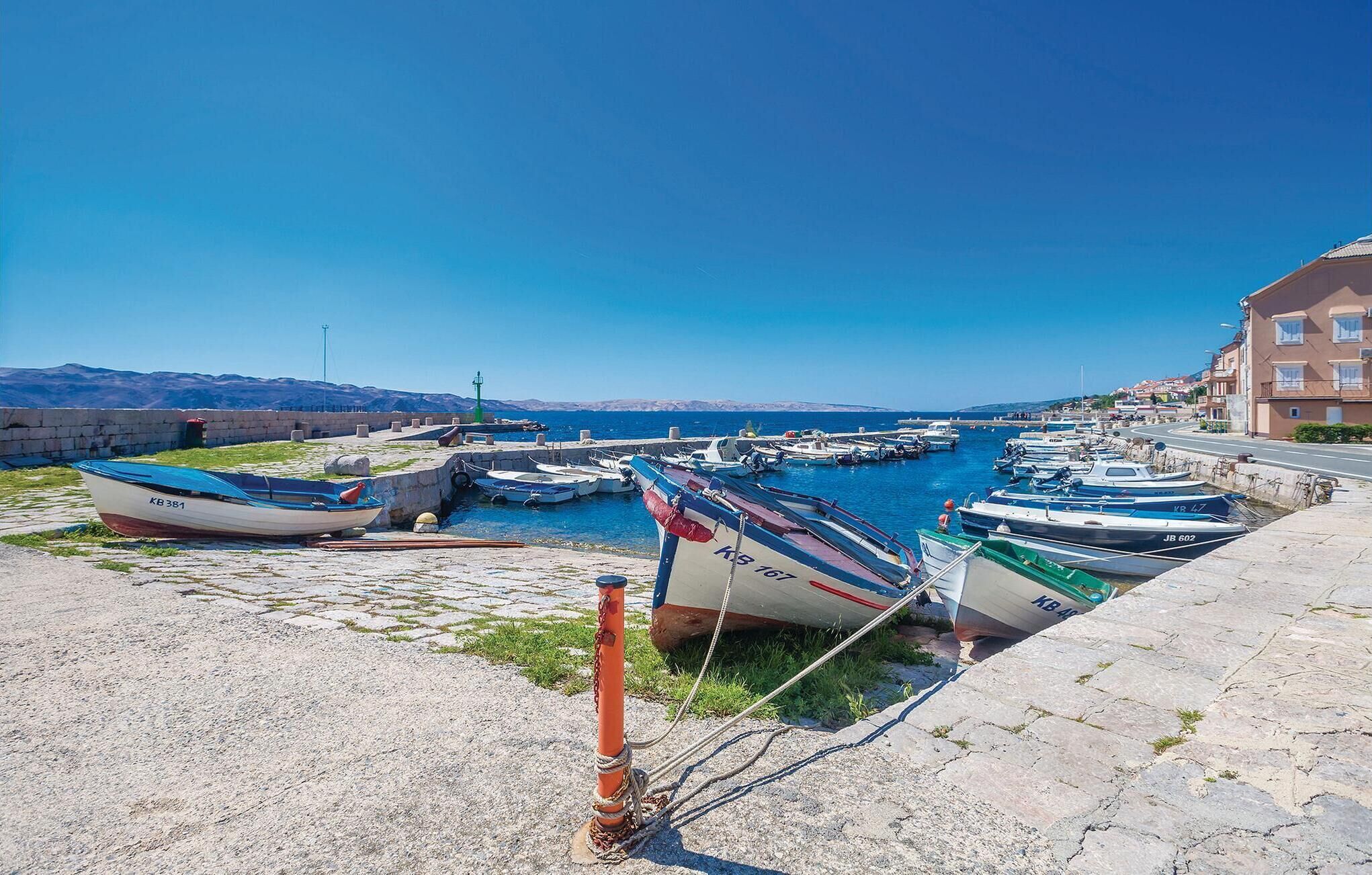 A harbor with boats docked, a stone wall, and buildings in the background.