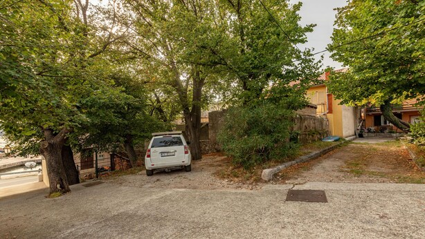A white car parked on a gravel driveway with trees and a building in the background. - Awesome apartment in Karlobag with WiFi (Karlobag)