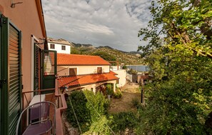 Ein Küstenhaus mit rotem Ziegeldach, einem Balkon mit Stuhl und Blick auf das Meer und die Berge.
