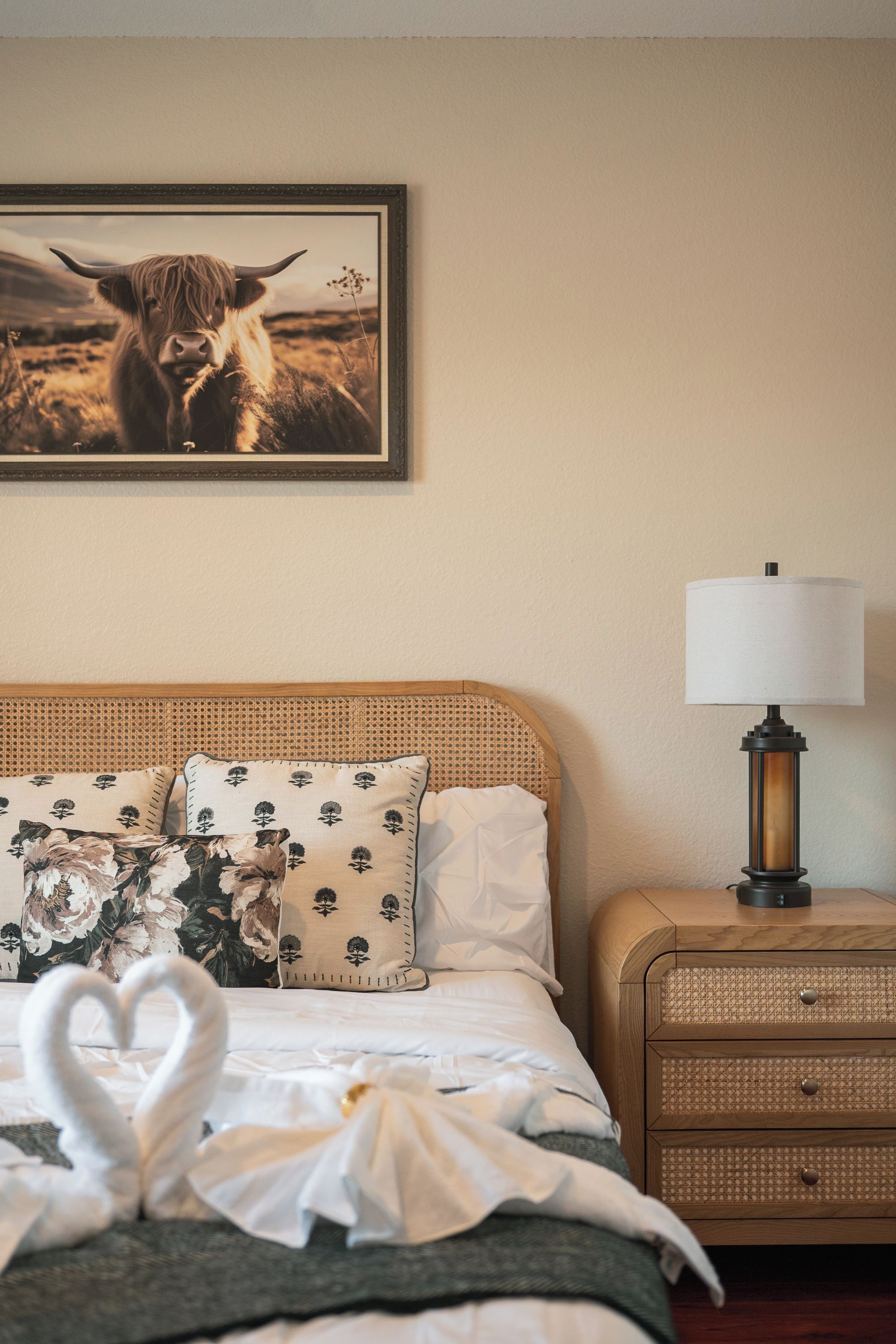 A hotel room with a bed, a nightstand, a lamp, and a framed picture of a cow on the wall.