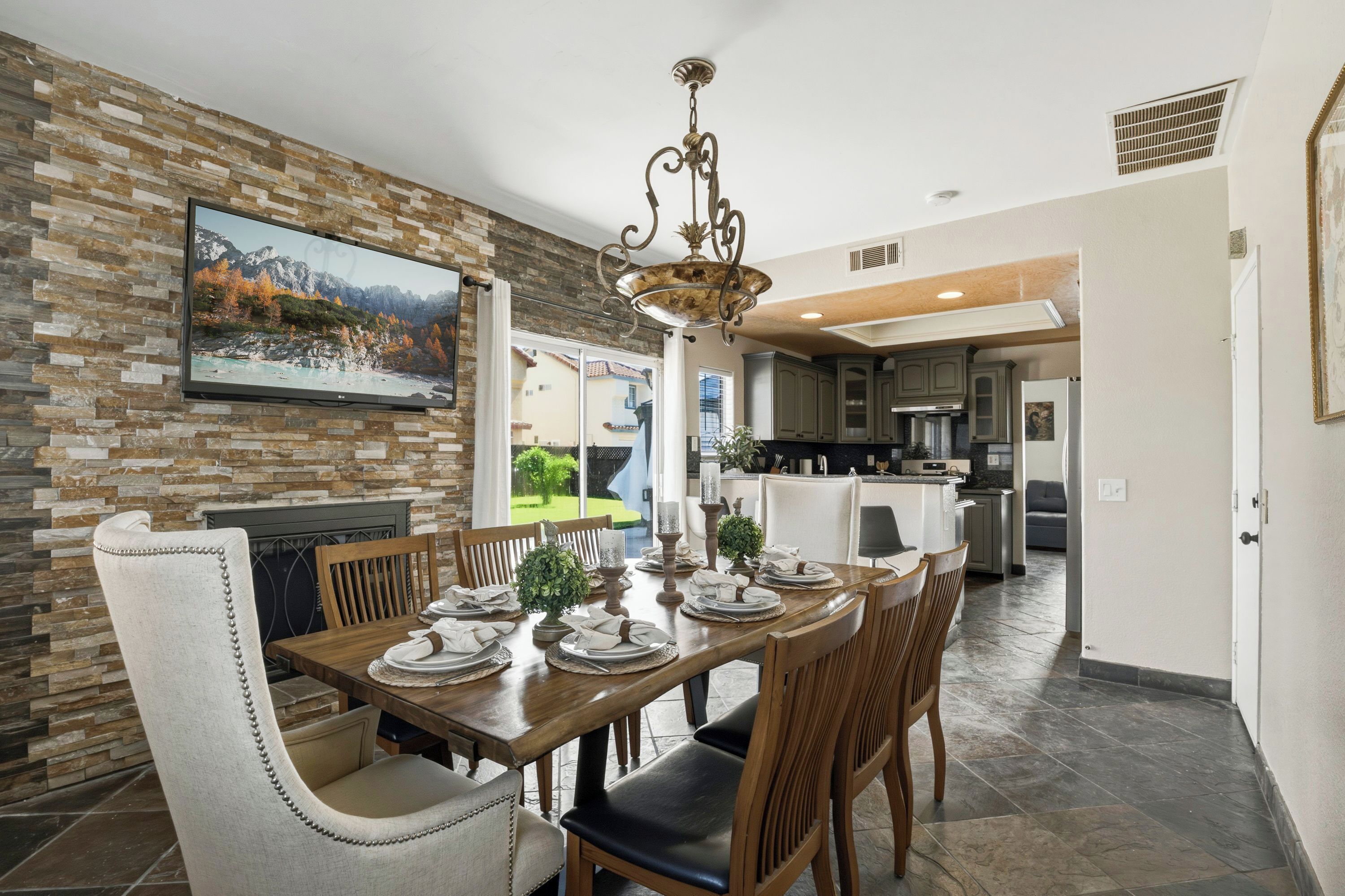 A dining area with a stone wall, a mounted TV, and a chandelier.
