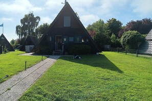 A triangular building with a porch and a paved path leading to it. - gemütliche Unterkunft in Burhave (Fedderwardersiel)