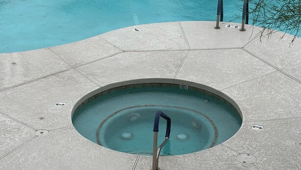 Una piscina circular con desagüe central, rodeada por una terraza con baldosas.