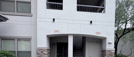 Un edificio residencial de dos plantas con entrada principal, dos balcones y base de piedra.
