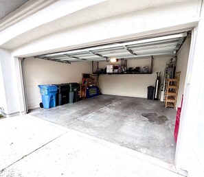 Eine Garage mit Betonboden, einer Metallgaragentür sowie verschiedenen Gegenständen wie Behältern, einer Leiter und einem Regaleinheit.
