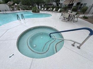 Une piscine avec un jacuzzi, des chaises longues et un espace salon abrité.