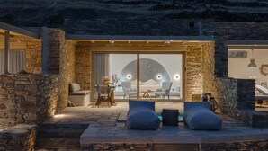 A stone-walled outdoor seating area with a pool, a dining table, and a view of the interior. - Fos Suite by Vivian Horizon Tinos, Vivian Suites Tinos (Tinos)